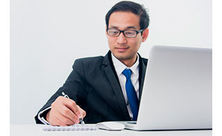 foto de um homem trabalhando num notebook e fazendo anotações num bloco de papel